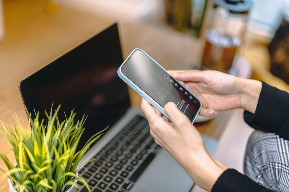 Woman holding smartphone above laptop in home office