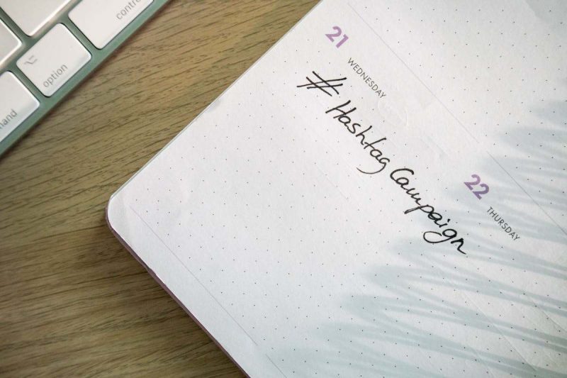 Open planner with hashtag campaign notes next to keyboard for social media marketing