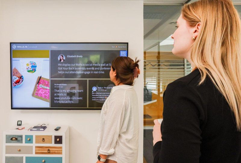 Two women analyzing social media metrics on wall display in office