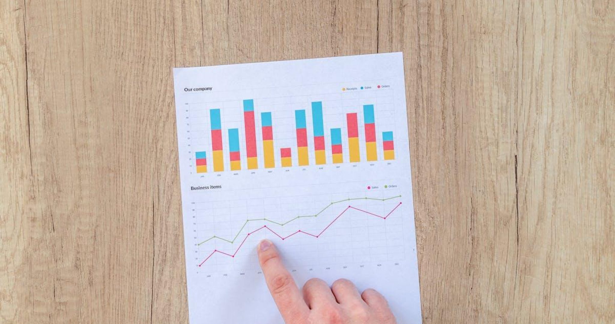 Hand pointing to colorful business charts showing revenue growth