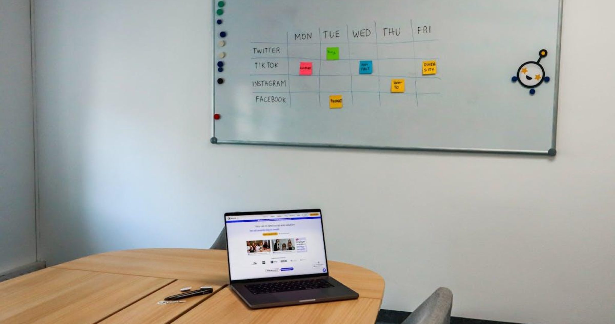 Laptop on conference table with organized whiteboard schedule showing social media automation workflow