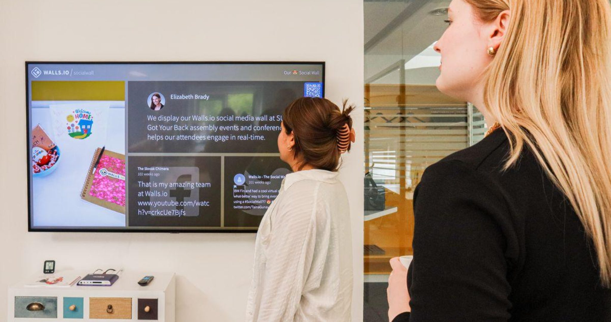 Two women analyzing social media metrics on wall display in office