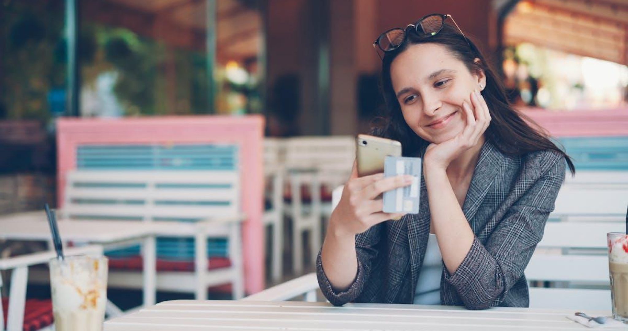 Smiling woman using smartphone and credit card at cafe for online shopping