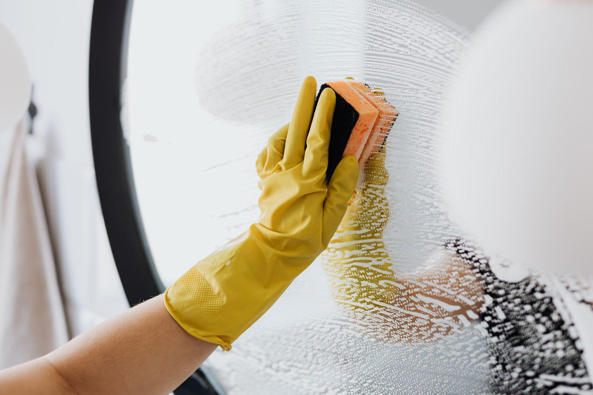 Person wearing yellow rubber gloves cleaning a bathroom mirror with a sponge