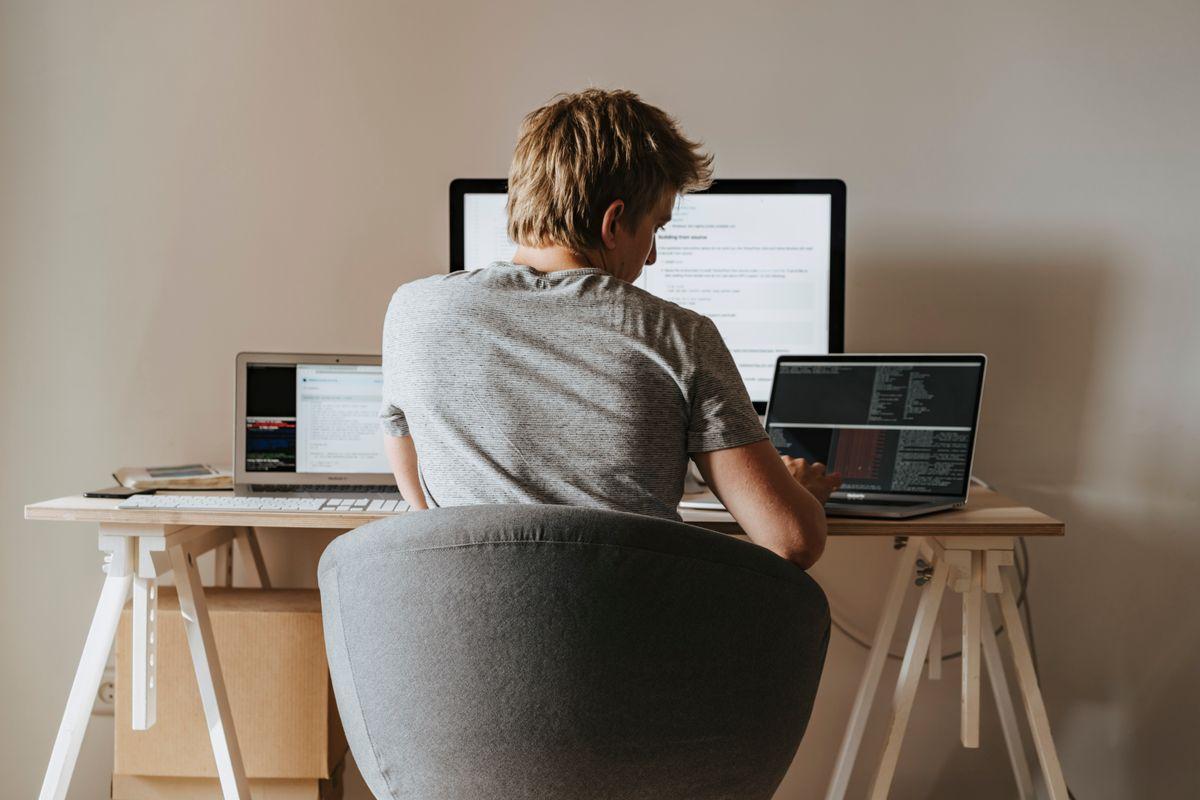 Young man working at home office with multiple laptops, representing remote work and multitasking