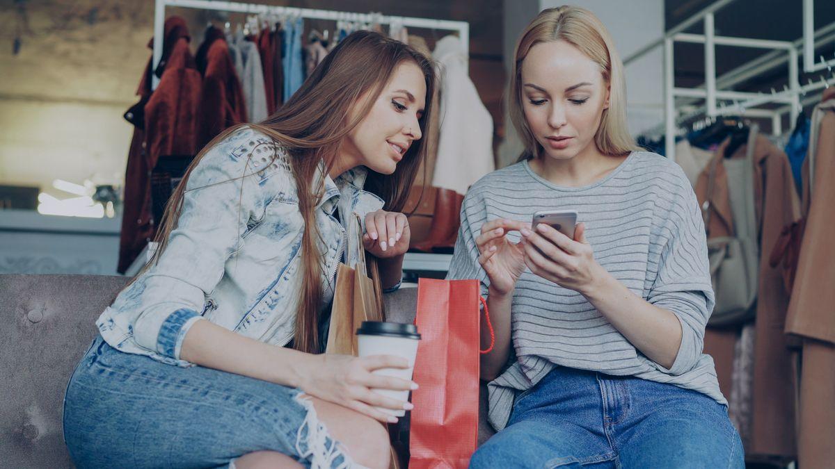 Two women shopping in a boutique while using a smartphone
