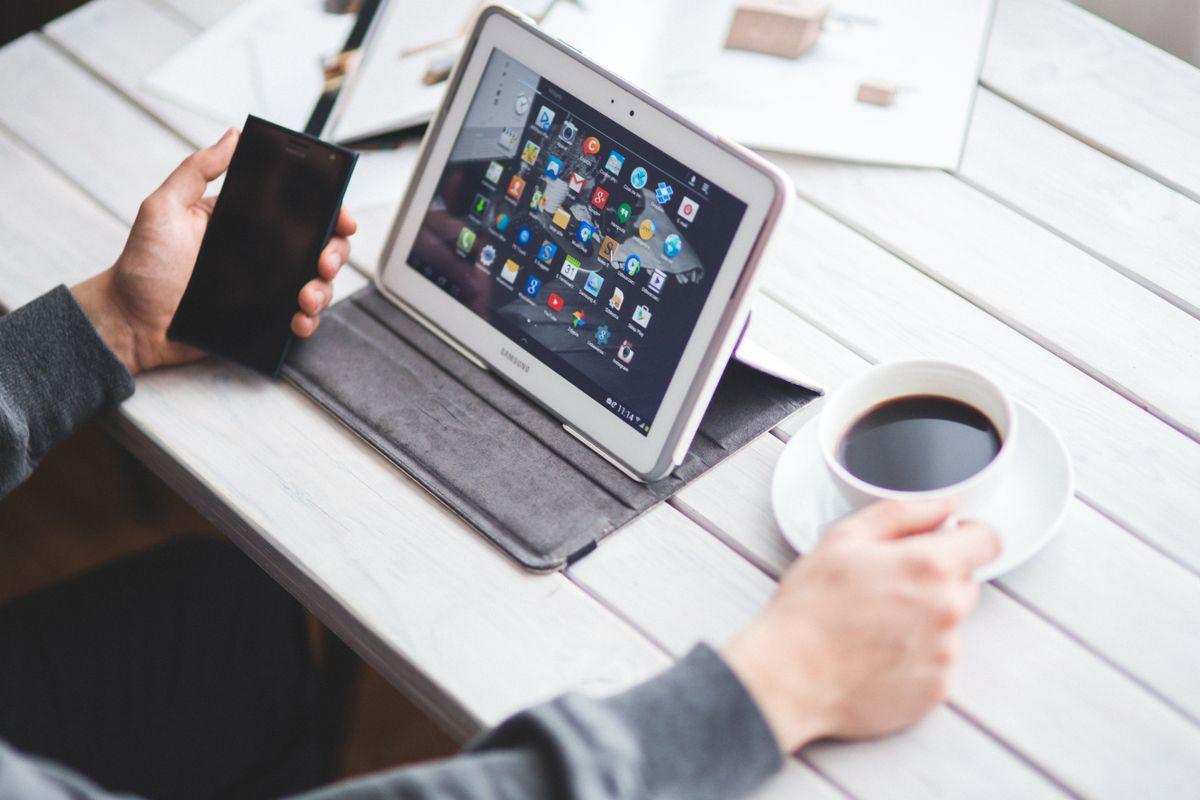 Person managing social media on tablet with coffee