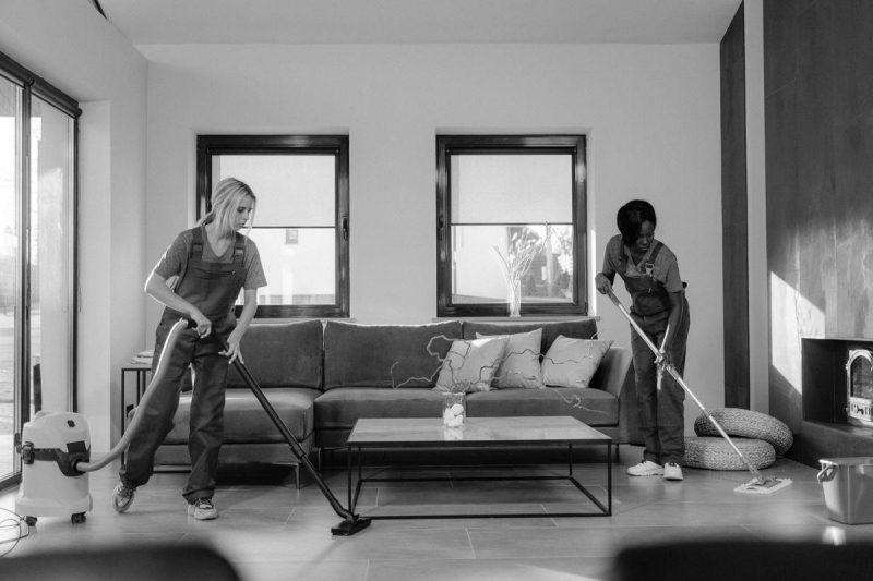 Two professional cleaners in work clothes vacuuming and mopping a modern living room