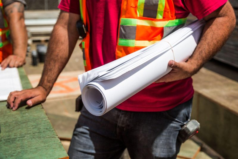 Construction workers in safety vests reviewing blueprints at a construction site