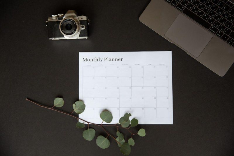 Monthly planner beside a camera and laptop for social media content planning