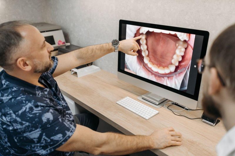 A dentist explaining dental conditions using images on a computer screen, representing modern dental technology