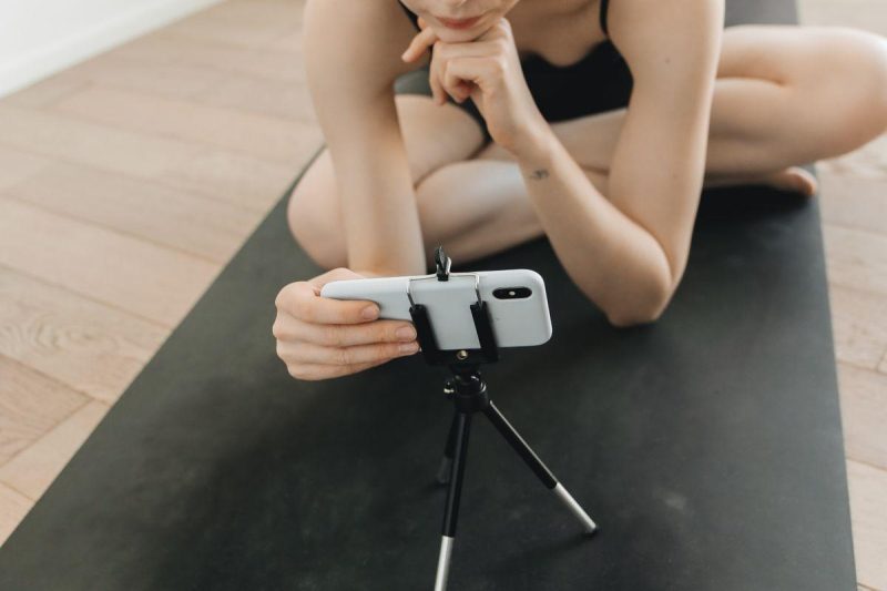 Woman in activewear filming fitness content with a smartphone and tripod indoors