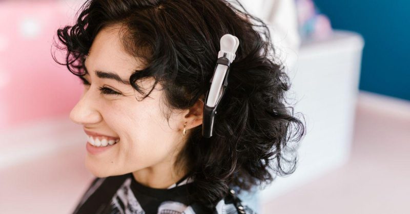 Side profile of a woman with curly hair smiling in a hair salon