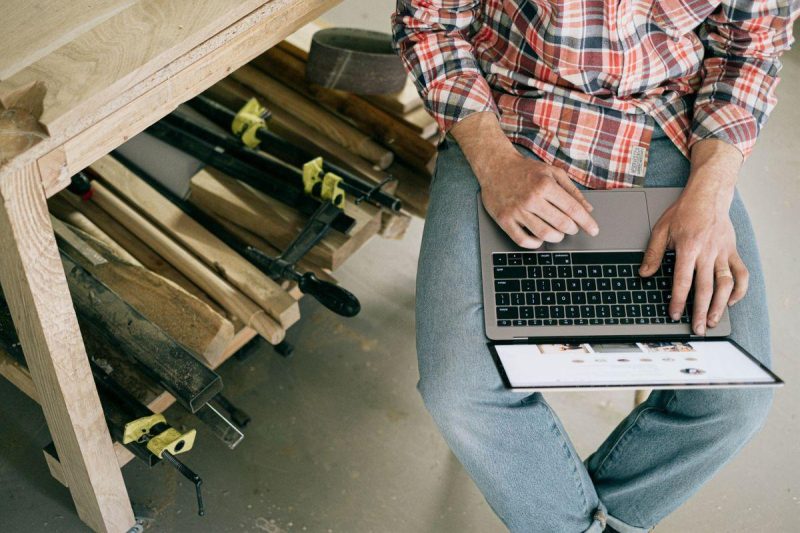 A craftsman using a laptop in a woodworking workshop