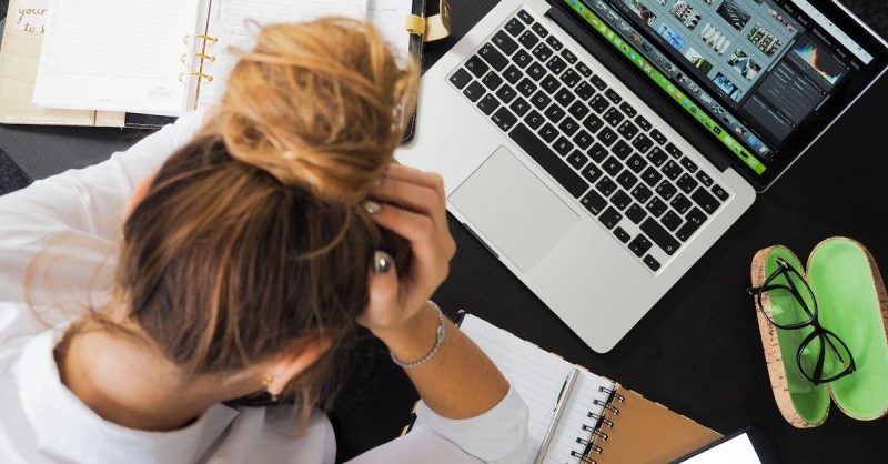 Overhead view of a stressed person working at a desk with a laptop, phone, and notebooks