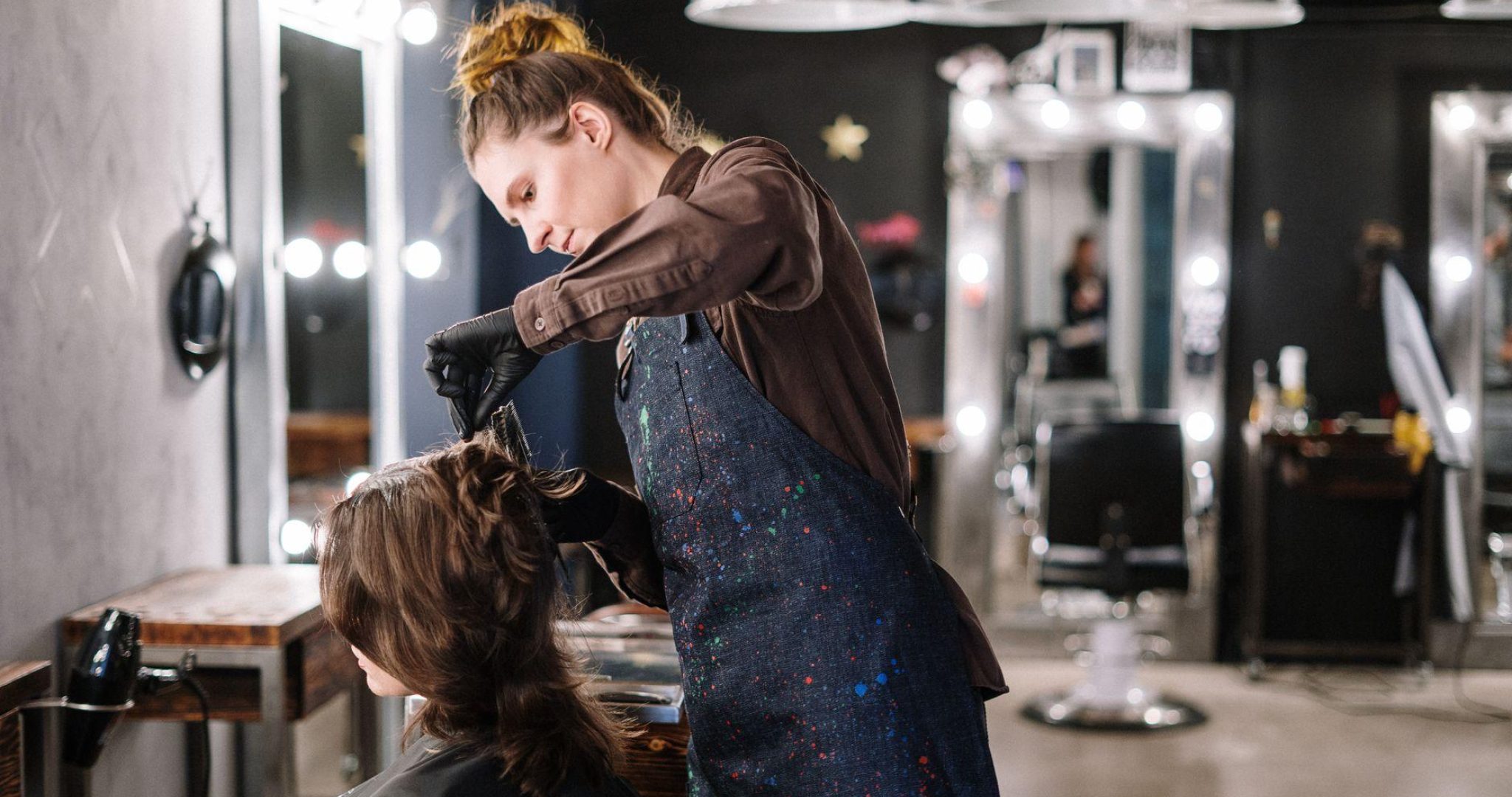 A female stylist expertly applying hair color to a client in a modern salon setting