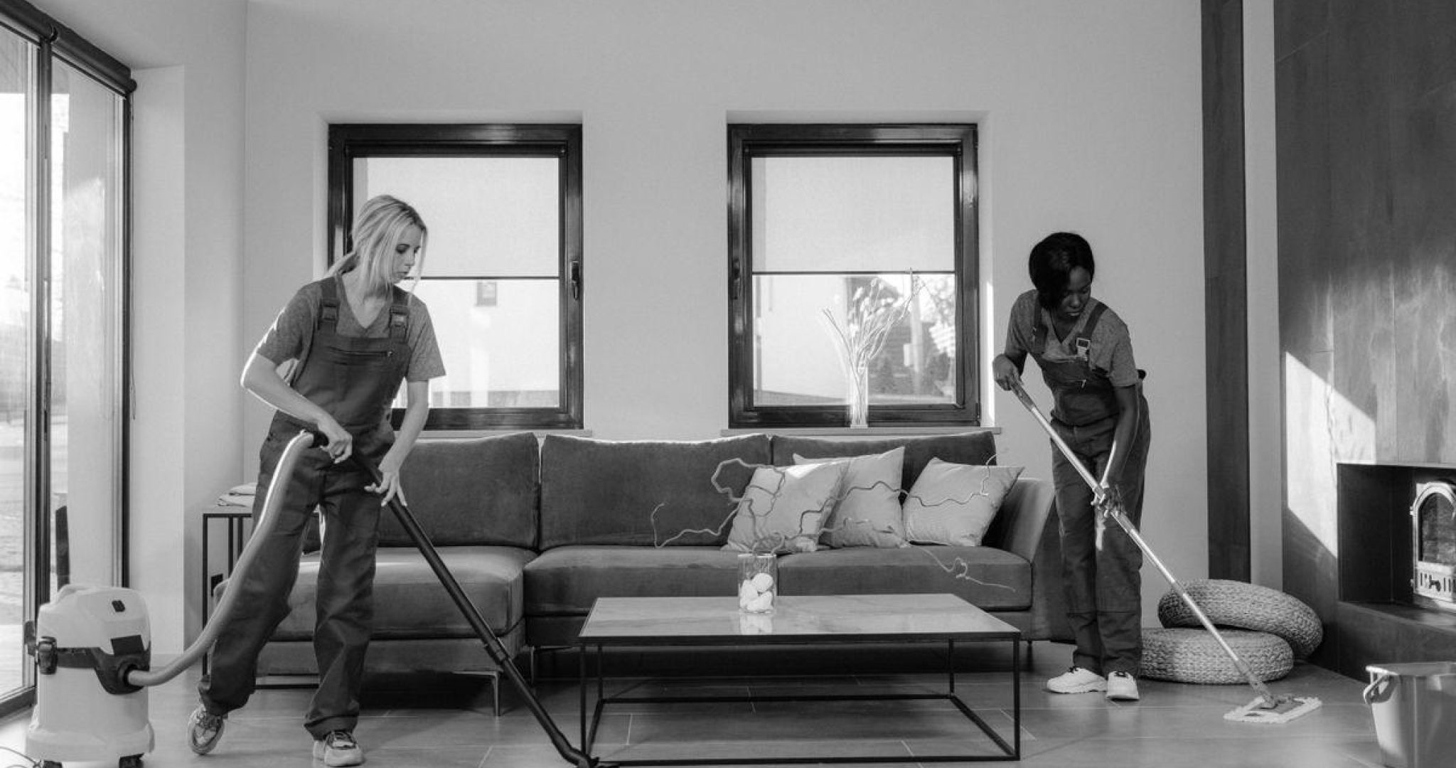 Two professional cleaners in work clothes vacuuming and mopping a modern living room