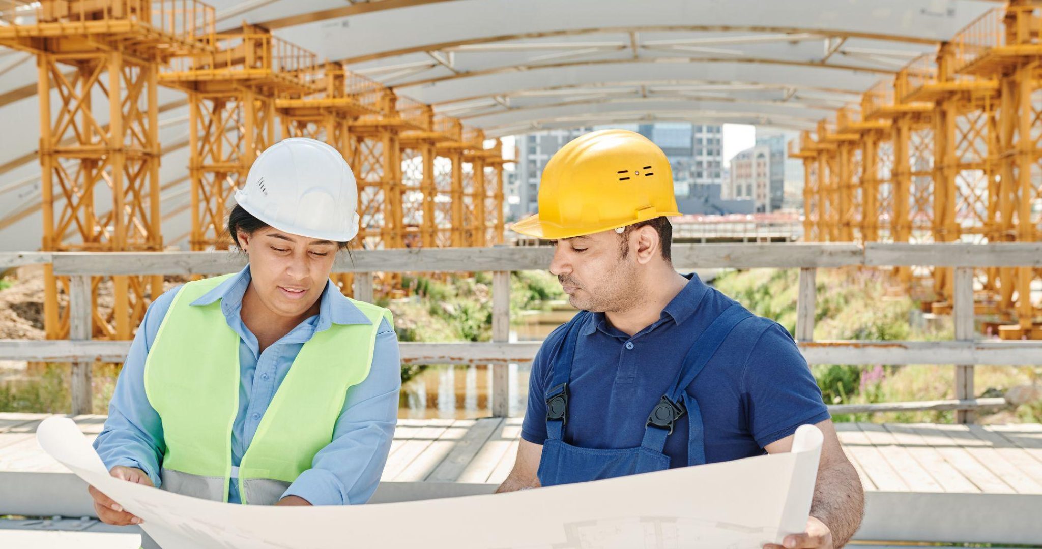 Engineering team in safety gear analyzing blueprints at outdoor construction site