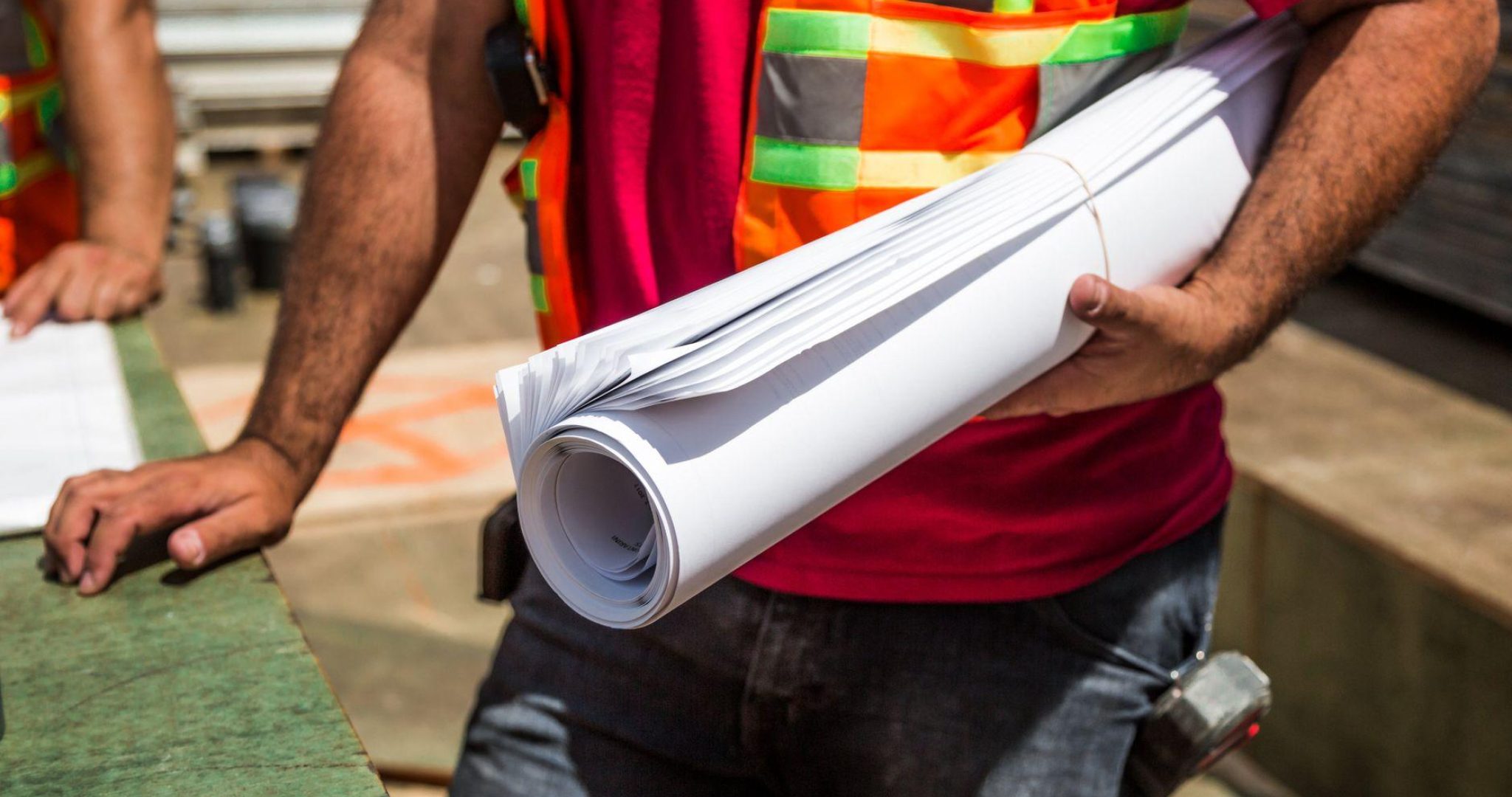 Construction workers in safety vests reviewing blueprints at a construction site