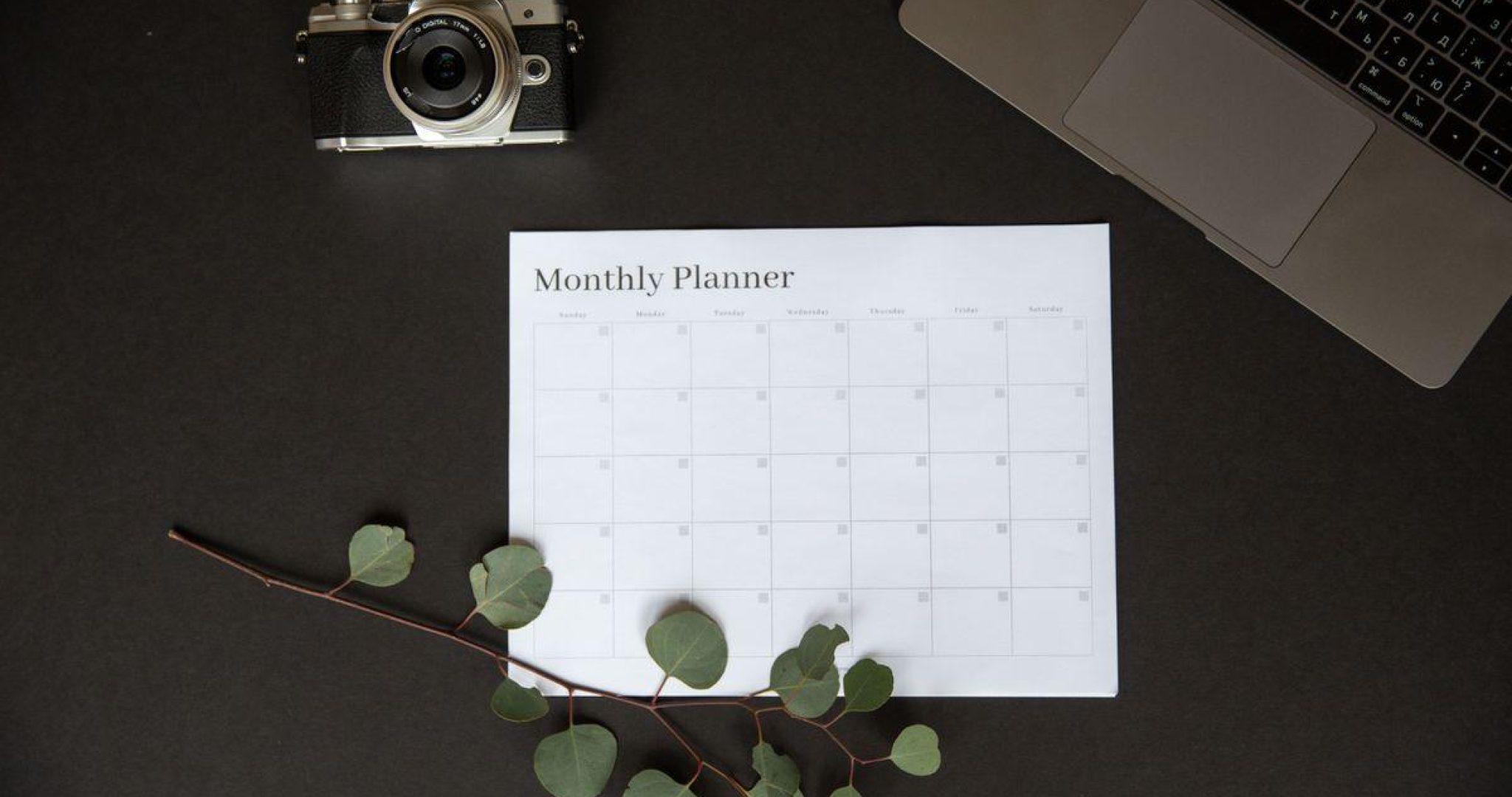 Monthly planner beside a camera and laptop for social media content planning