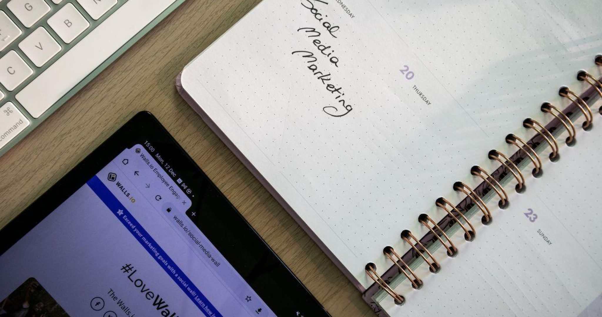 Overhead view of a notebook, tablet, and keyboard used for planning social media content
