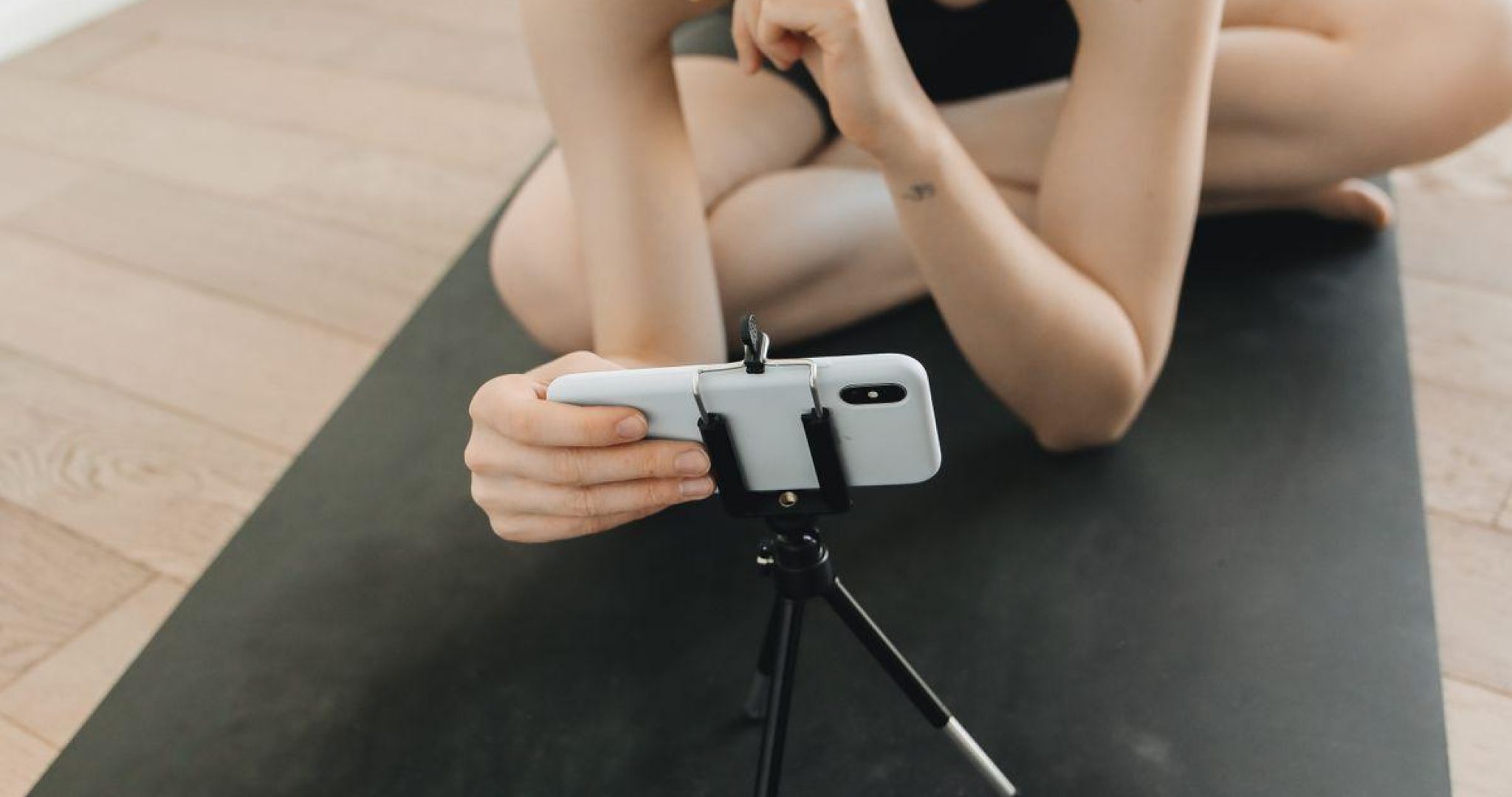 Woman in activewear filming fitness content with a smartphone and tripod indoors