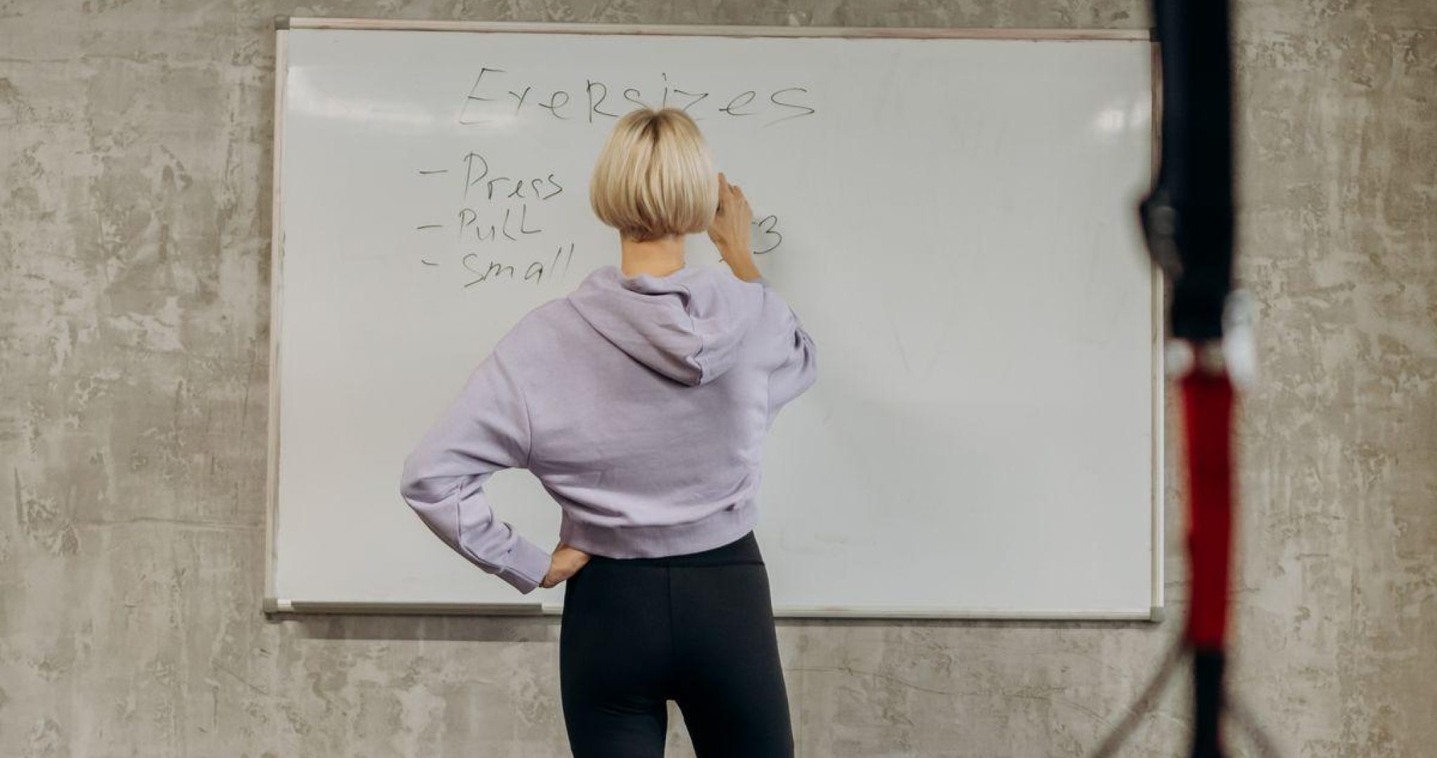 Female fitness instructor writing exercises on a whiteboard in a gym, planning the weekly workout schedule