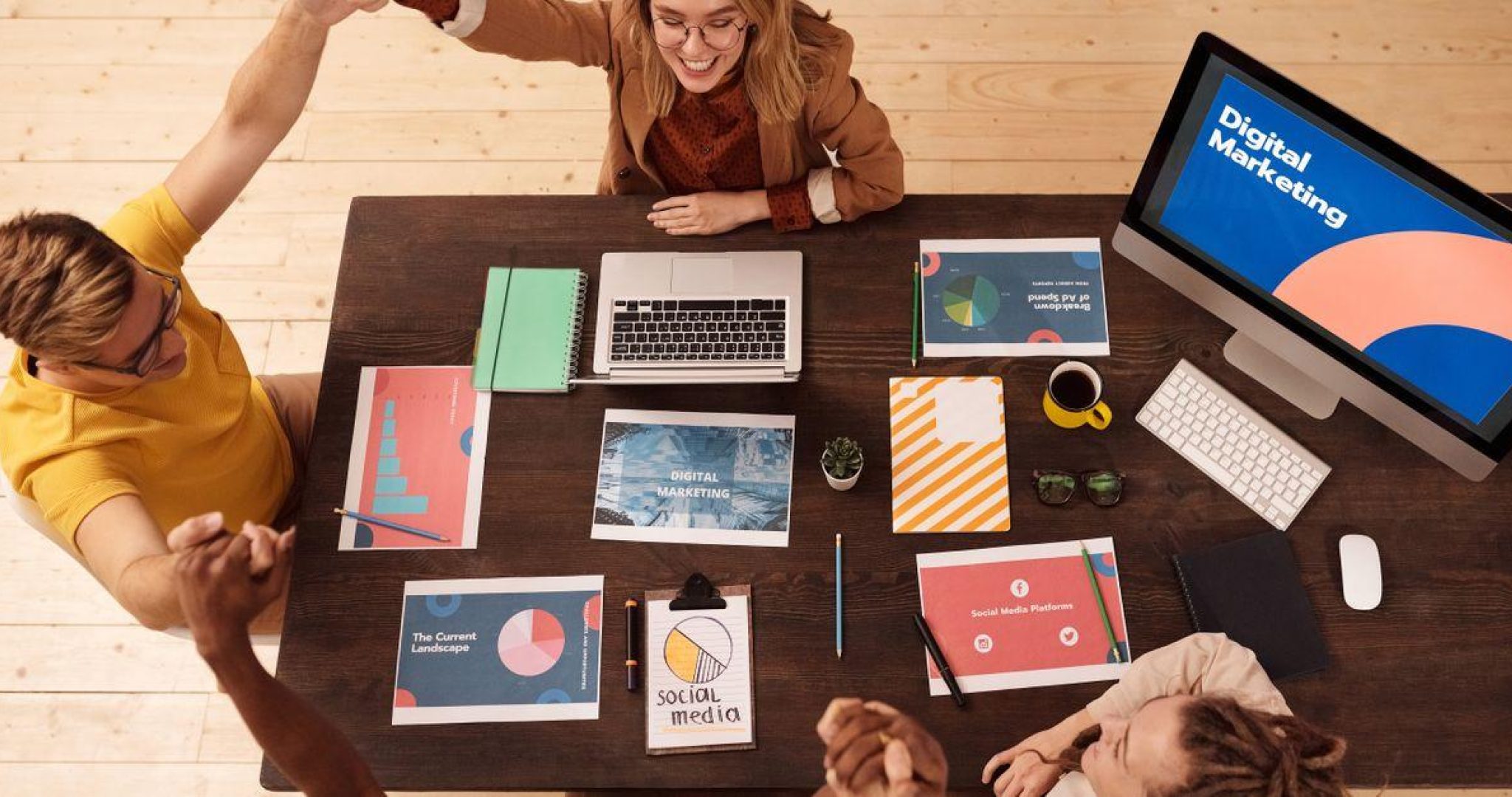 Marketing team collaborating around a desk in a modern office with laptops and screens showing social media analytics