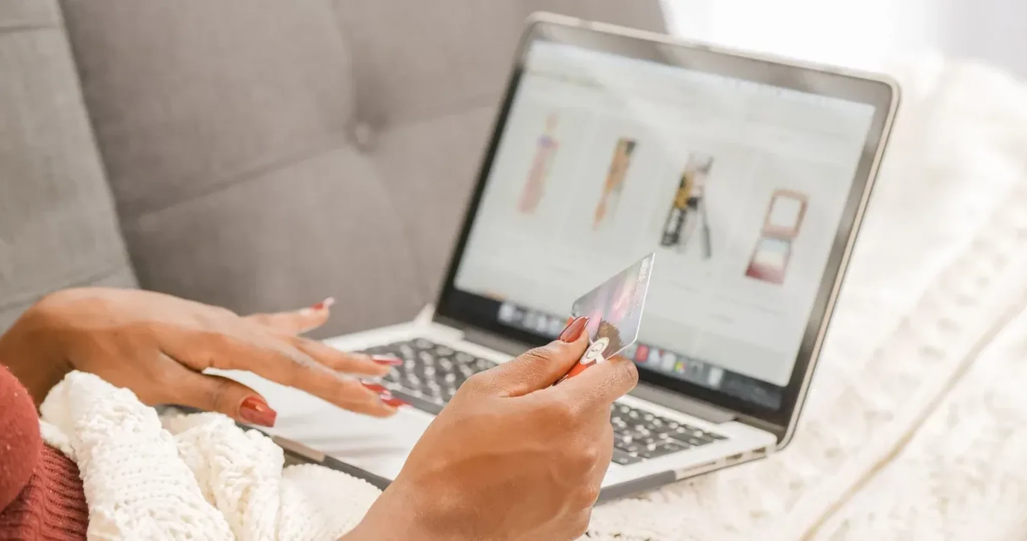 Woman sitting on a couch with a laptop, completing an online purchase with a bank card