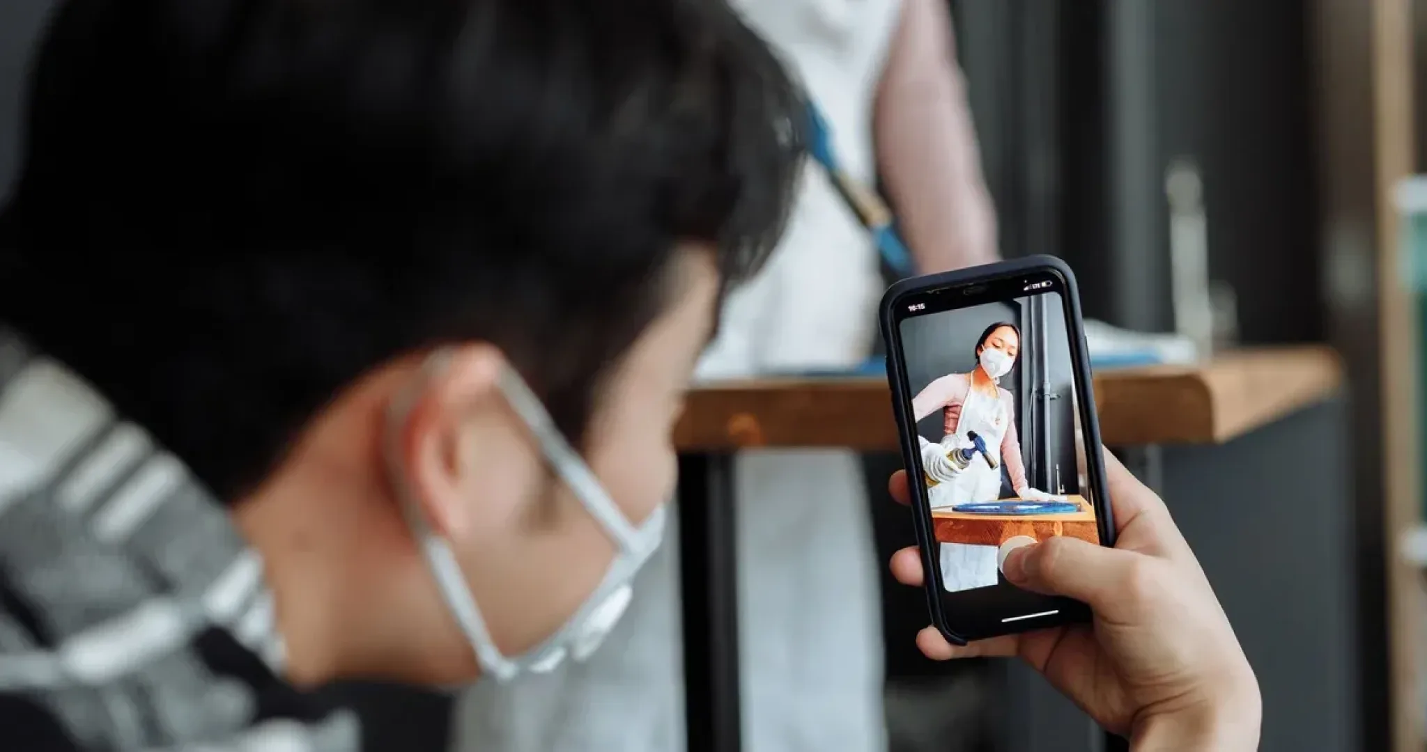 A person photographs a chef using a smartphone with a blurred background, highlighting modern culinary art.