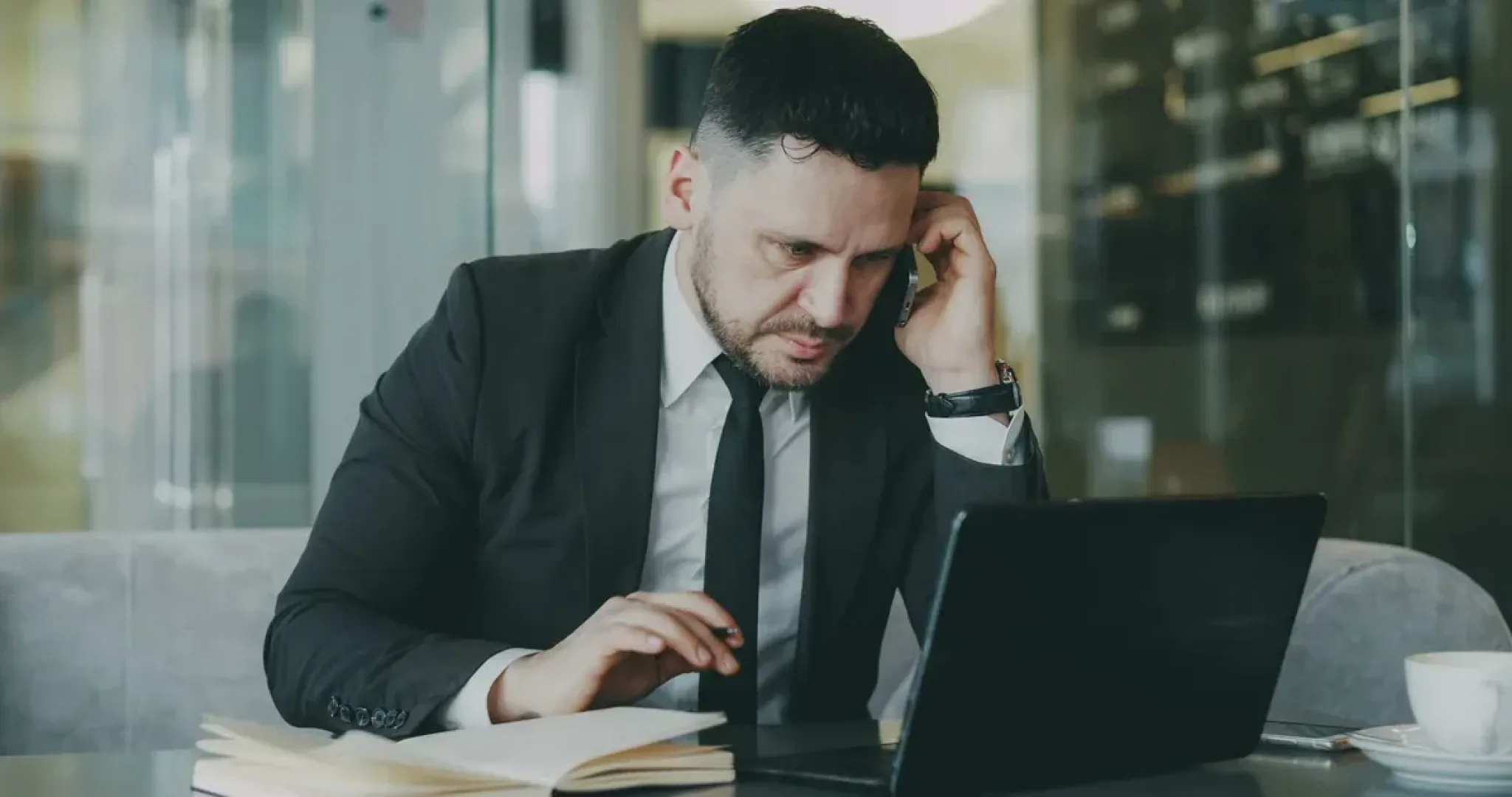 Focused professional multitasking on a phone and laptop at a modern office desk