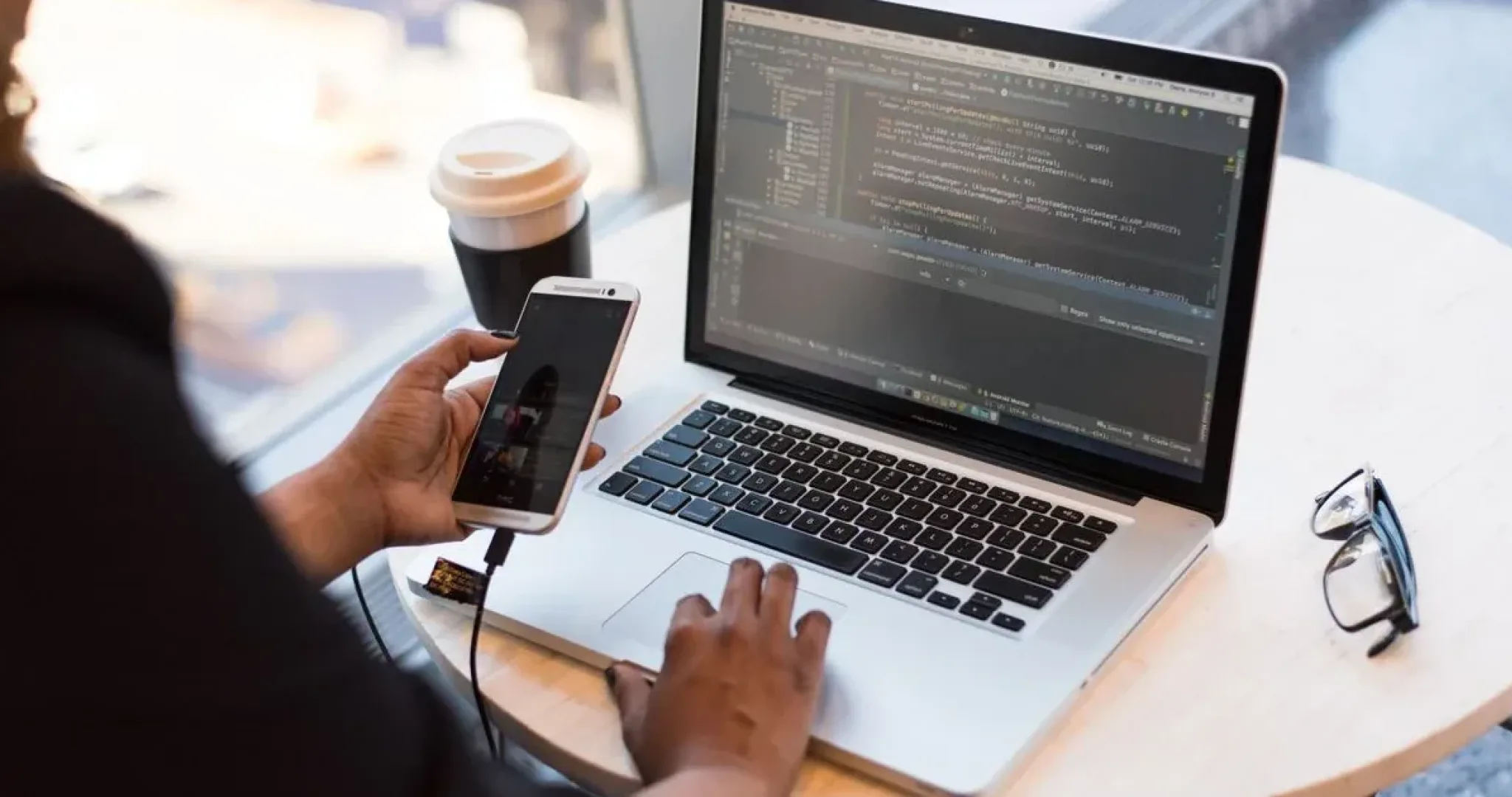 Remote worker checking a social media app on a smartphone while working on a laptop