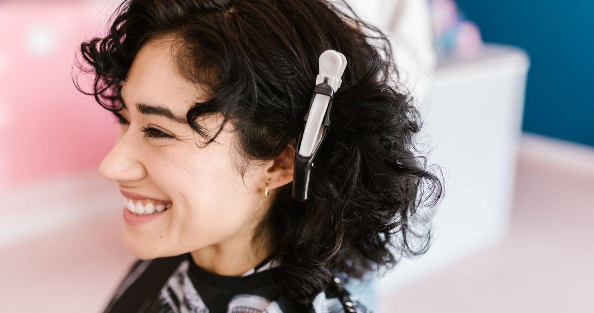 Side profile of a woman with curly hair smiling in a hair salon