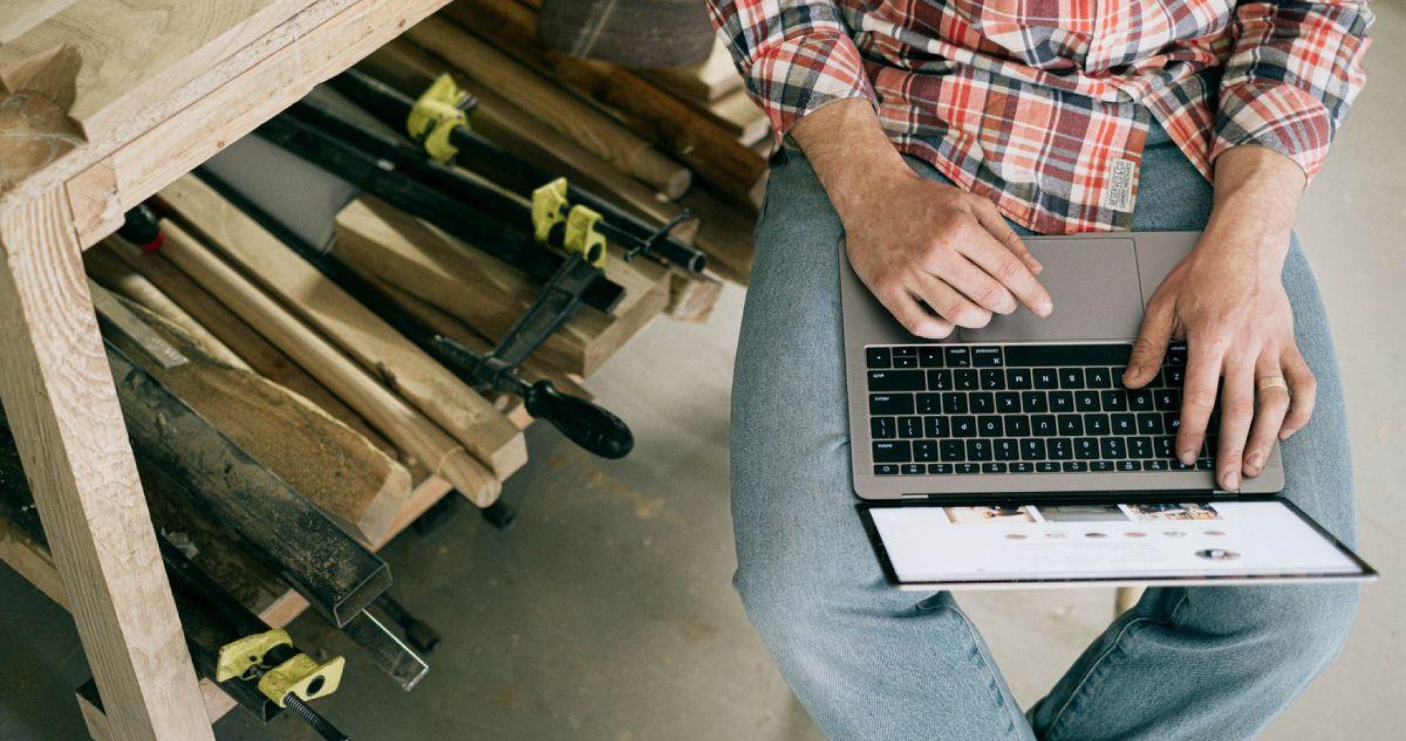 A craftsman using a laptop in a woodworking workshop
