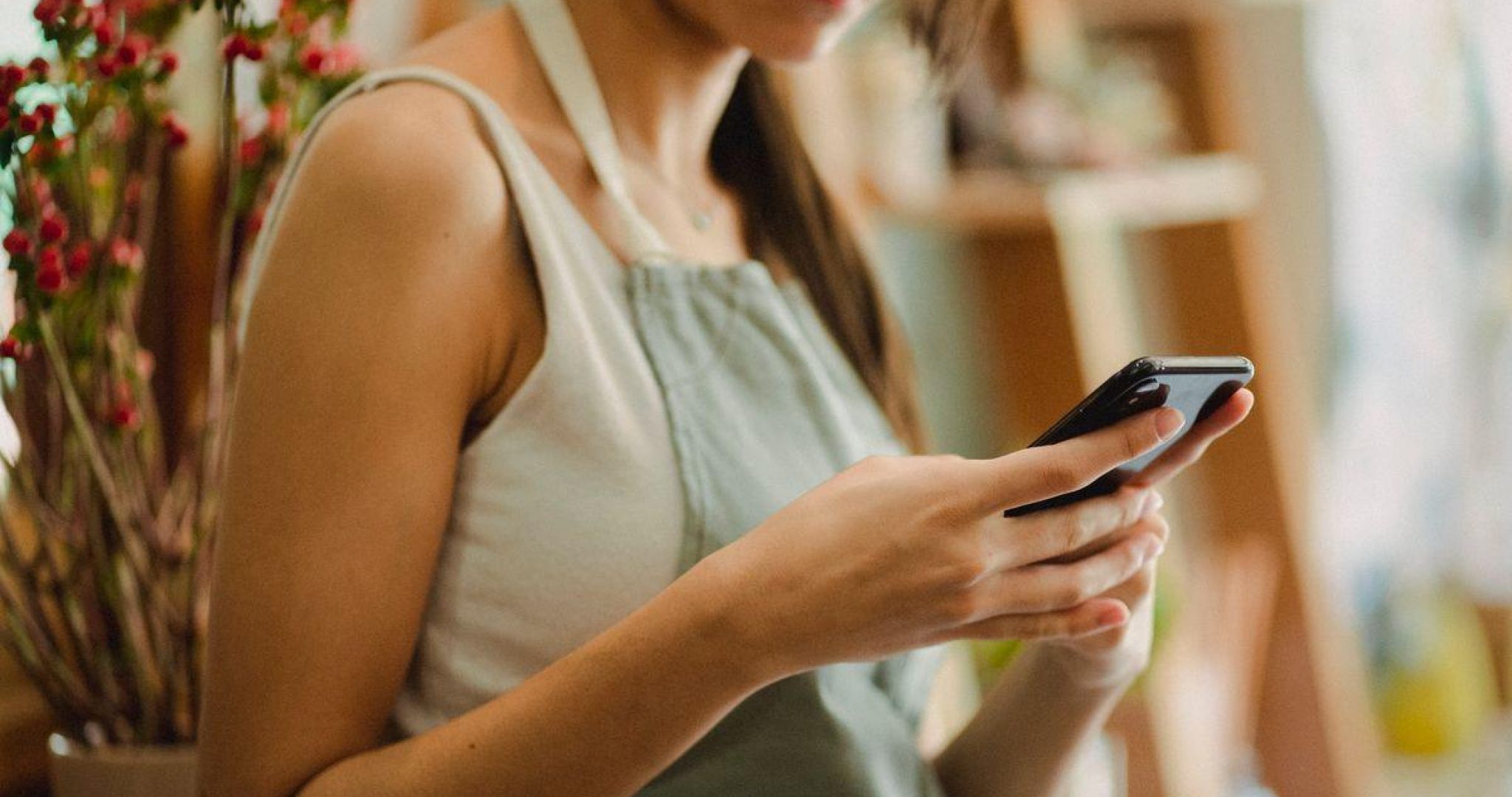 Florist in apron browsing mobile phone while working in floral shop
